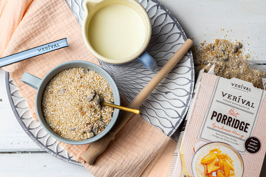 Un bol de porridge avec une cuillère, un pot de lait, un paquet de porridge aux abricots et au miel Verival et du porridge renversé sur un plateau avec une serviette.