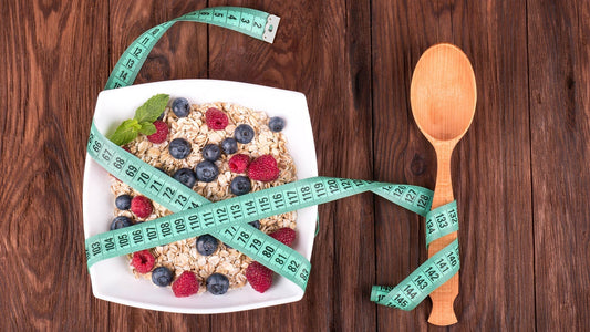 Un bol de porridge aux myrtilles et aux framboises, enveloppé d'un ruban à mesurer, se trouve à côté d'une cuillère en bois sur une surface en bois.