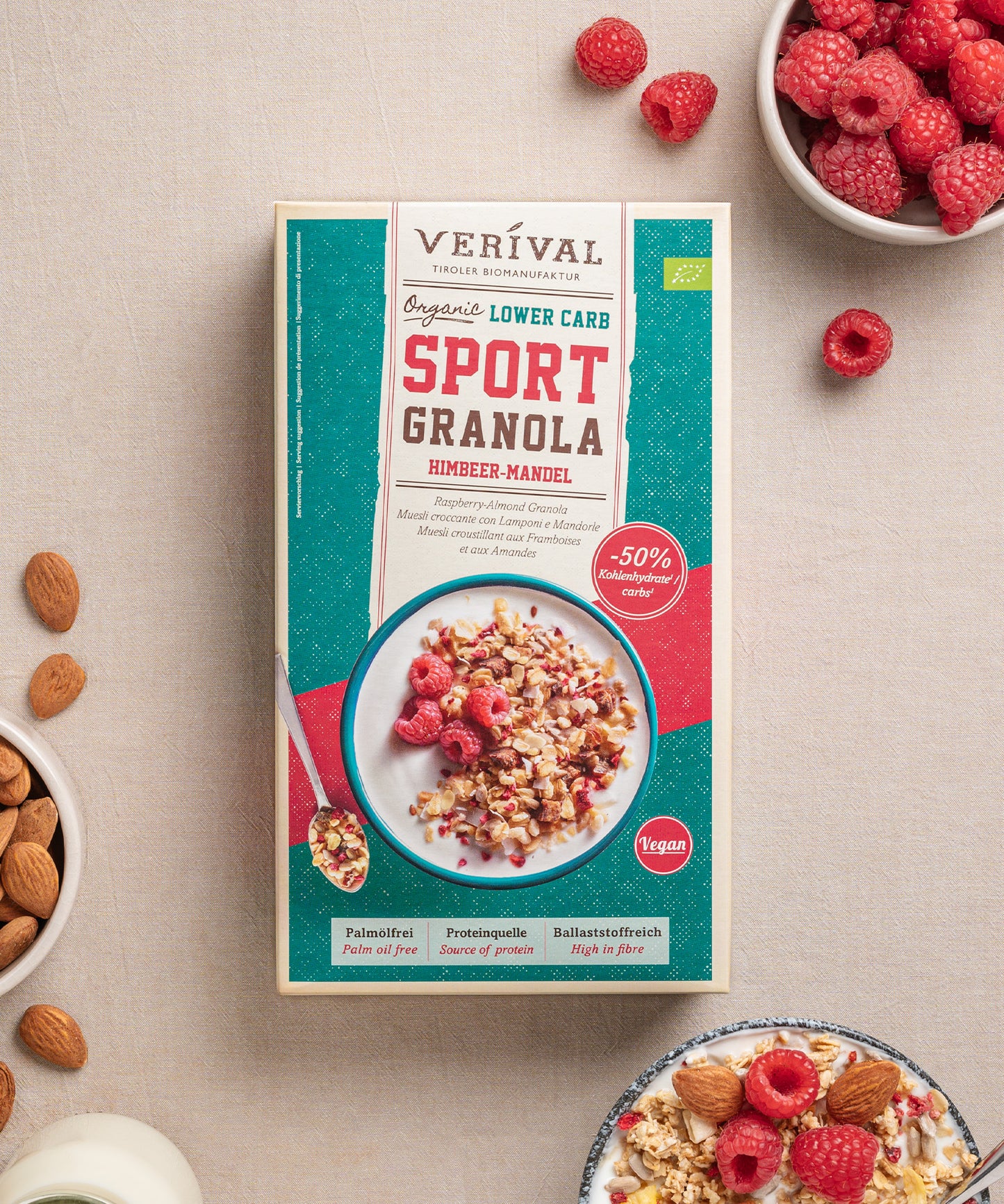 Eine Packung Protein Lower Carb Granola Himbeer-Mandel von Verival Bio, umgeben von kleinen Schalen mit Himbeeren und Mandeln. Vollgepackt mit pflanzlichem Protein unterstützt diese leckere Low-Carb-Option einen aktiven Lebensstil, ohne auf Geschmack zu verzichten.