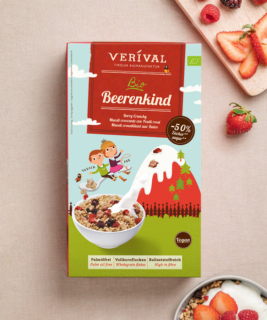 Das Paket Beerenkind von Verival Bio ist ideal für ein nahrhaftes Frühstück. Die Verpackung zeigt Cartoon-Kinder beim Wandern mit Müsli und Beeren. Daneben steht eine Schüssel veganes Müsli mit Milch, umgeben von frischen, ballaststoffreichen Beeren.