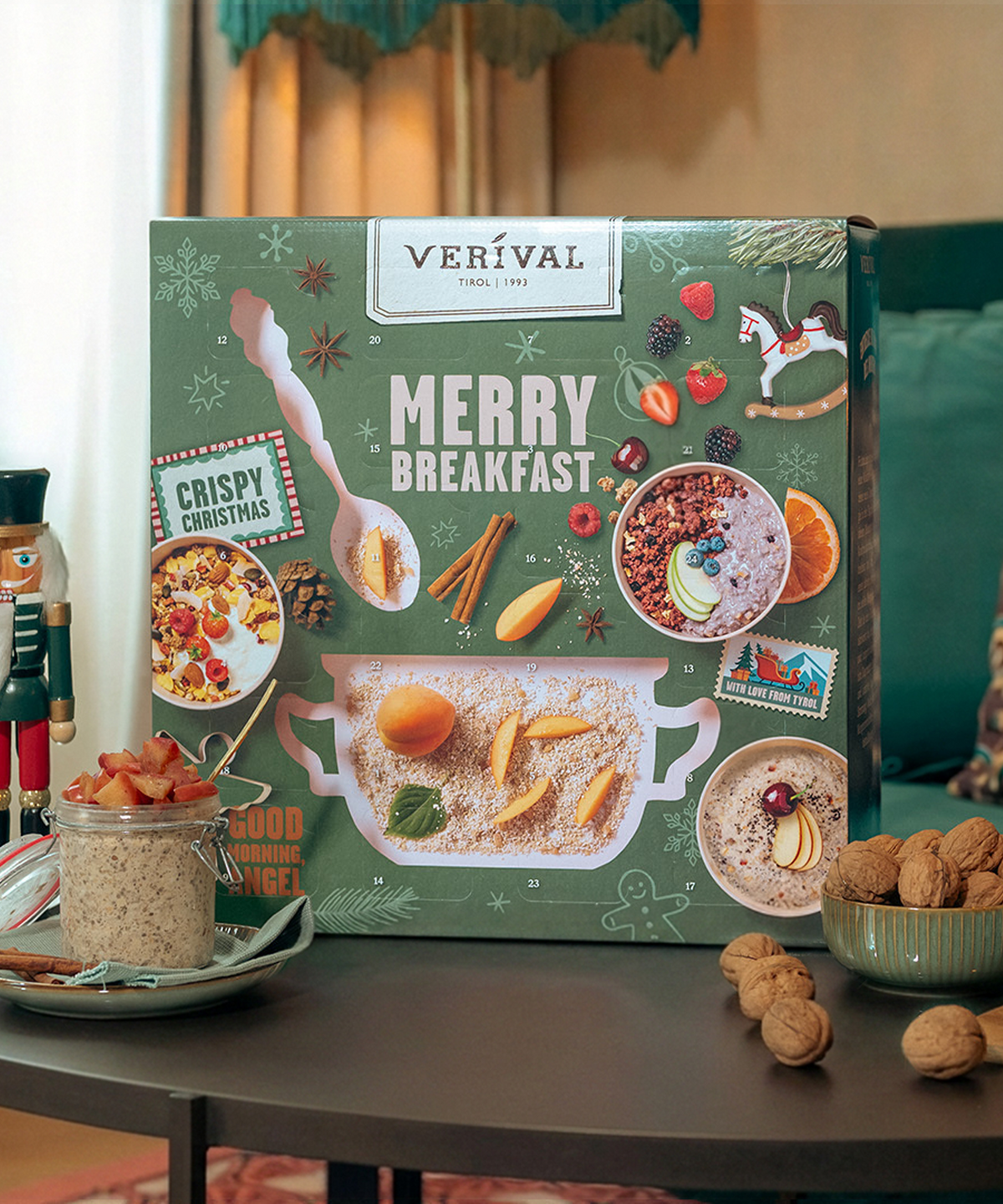 Auf einem Tisch steht eine festlich gestaltete Adventskalender-Box der Verival Bio GmbH, daneben eine Schüssel mit Müsli, Apfelscheiben, Walnüssen, einem Nussknacker und weihnachtlicher Dekoration, die im Hintergrund an einen Adventskalender erinnert.