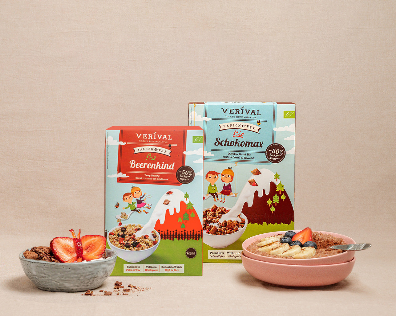 Zwei Packungen Verival-Müsli stehen hinter Schüsseln mit zubereitetem Müsli, garniert mit Früchten, auf einem beigen Hintergrund.