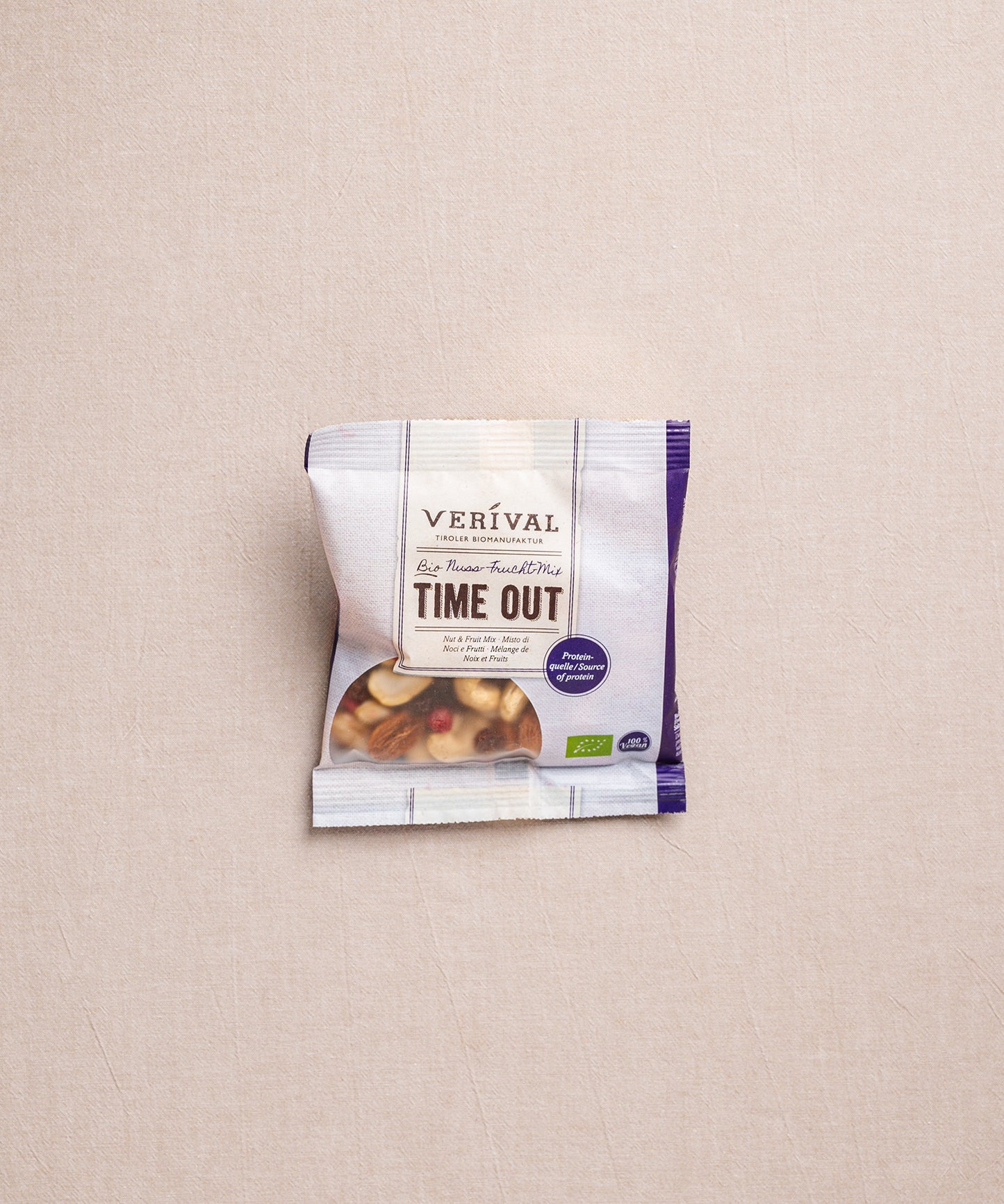 Ein Verival Bio GmbH Set "Protein Breakfast" Snack-Packung mit sichtbaren gemischten Nüssen, ideal für Bio-Sportnahrung oder ein proteinreiches Frühstück, platziert auf einer neutralen beigen Oberfläche.